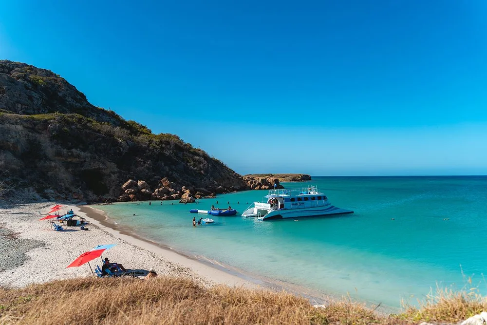 A boat at the turquoise waters and beach of Caja de Muertos
